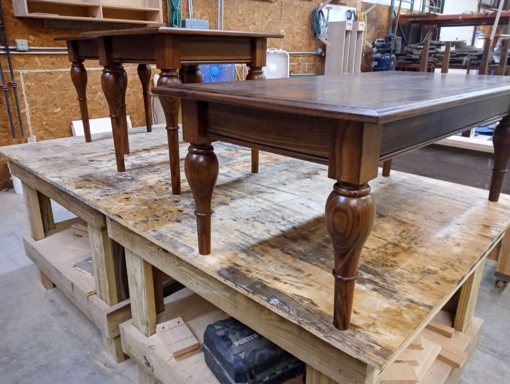 Three finished wooden tables of varying sizes on a workbench, likely in a workshop.