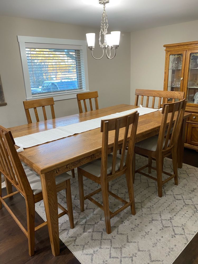 Dining room with wood table, six chairs, rug, and hutch. A chandelier hangs above the table.