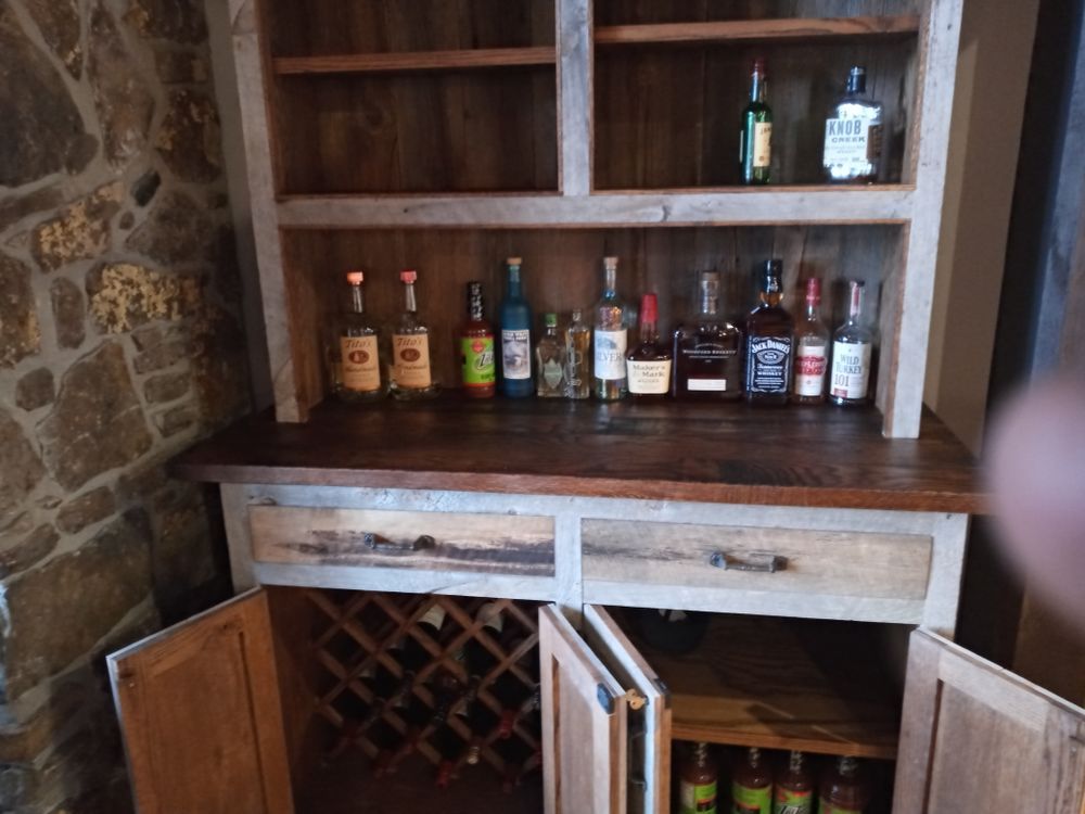 Rustic wooden liquor cabinet with open doors, holding bottles and wine rack, set against a stone wall.