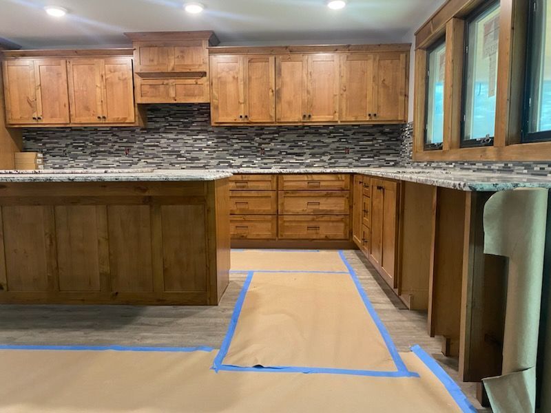 Kitchen remodel in progress, featuring wood cabinets, stone backsplash, and covered flooring.