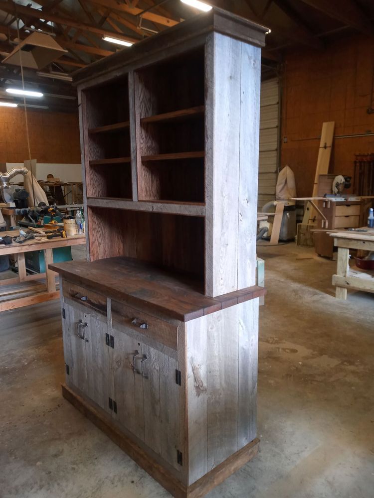 Wooden cabinet with shelves, two doors, and dark wooden top, in a workshop.