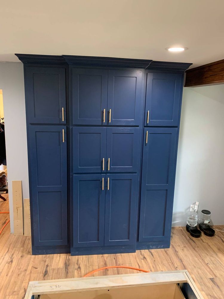 Blue kitchen cabinets with gold handles against a light blue wall, on wood floor.