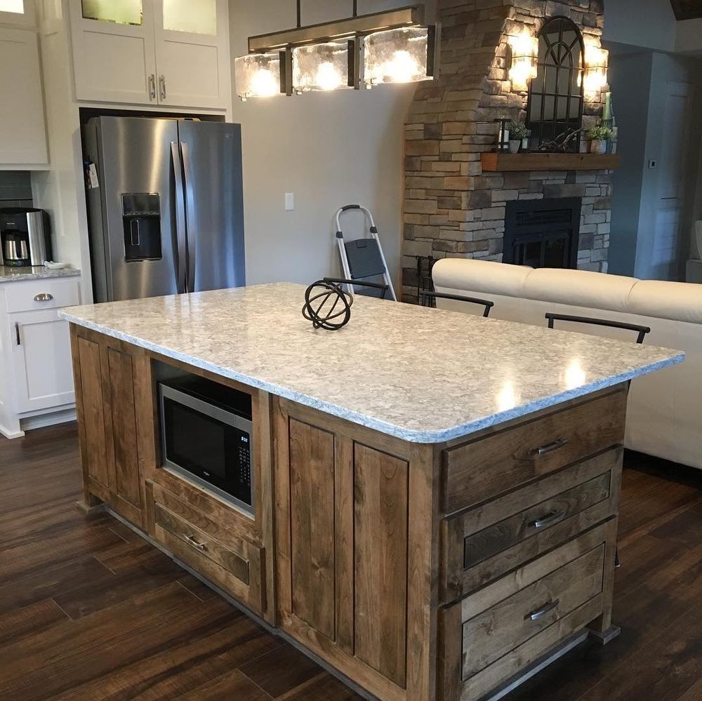 Kitchen island with granite countertop, built-in microwave, wood cabinets, and stainless steel refrigerator.
