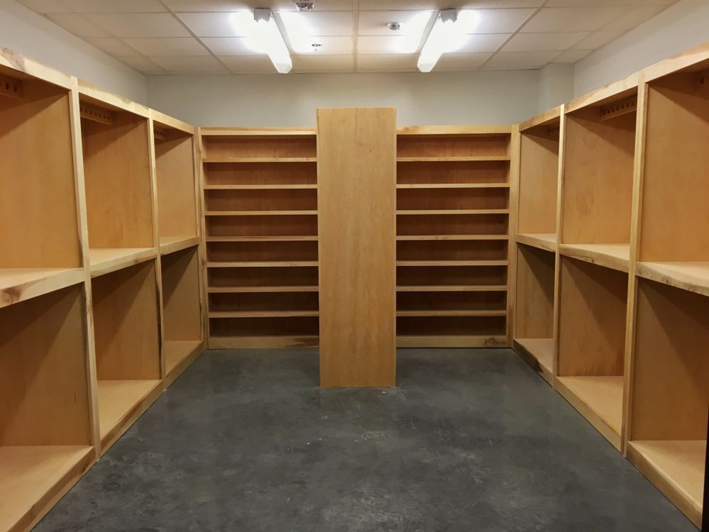 Empty wooden bookshelves line the walls of a room. A central divider splits the space.