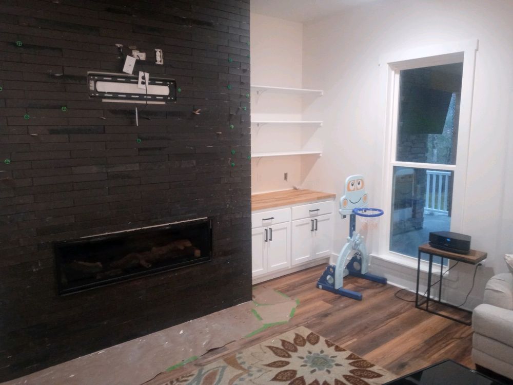 Living room with black tile fireplace, built-in shelves, window, exercise bike, and wood-look flooring.