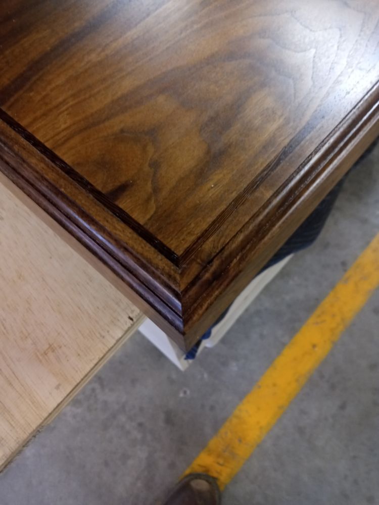 Close-up of a wood surface with a dark finish, showcasing the details of a decorative border, and a yellow tool handle.