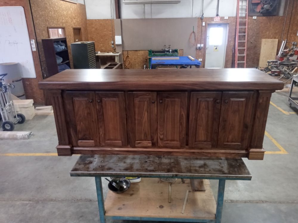 Dark wooden cabinet with six doors, set on a metal table, in a workshop.