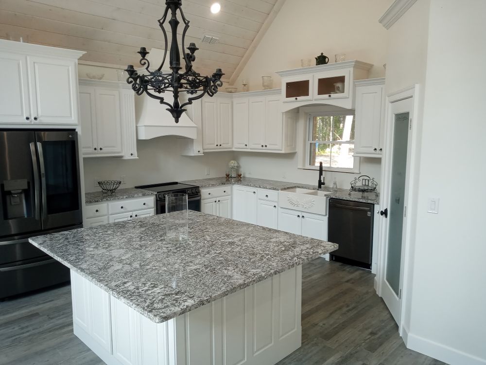 White kitchen with granite island, black chandelier, and stainless steel appliances.