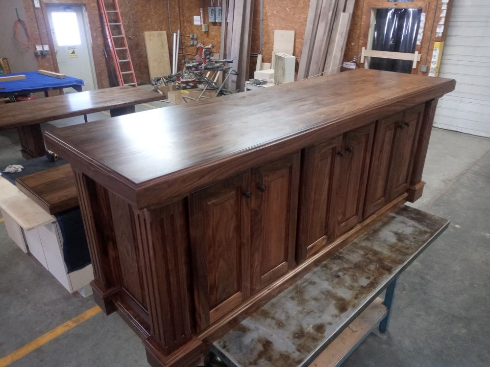 Wooden bar with cabinet doors, brown stain, on a workbench in a workshop.