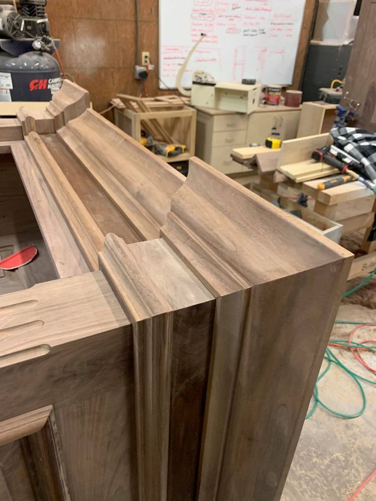 Close-up of unfinished wooden cabinet corner with ornate molding in a workshop setting.