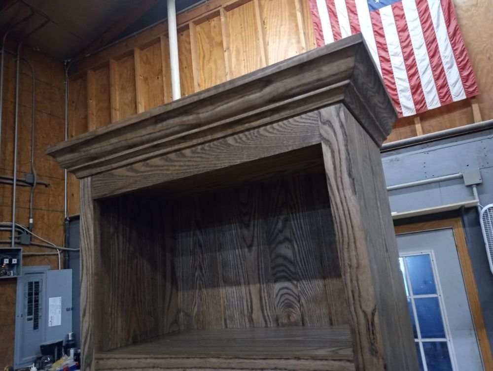 Wooden cabinet with open shelf; brown stained; American flag in the background.