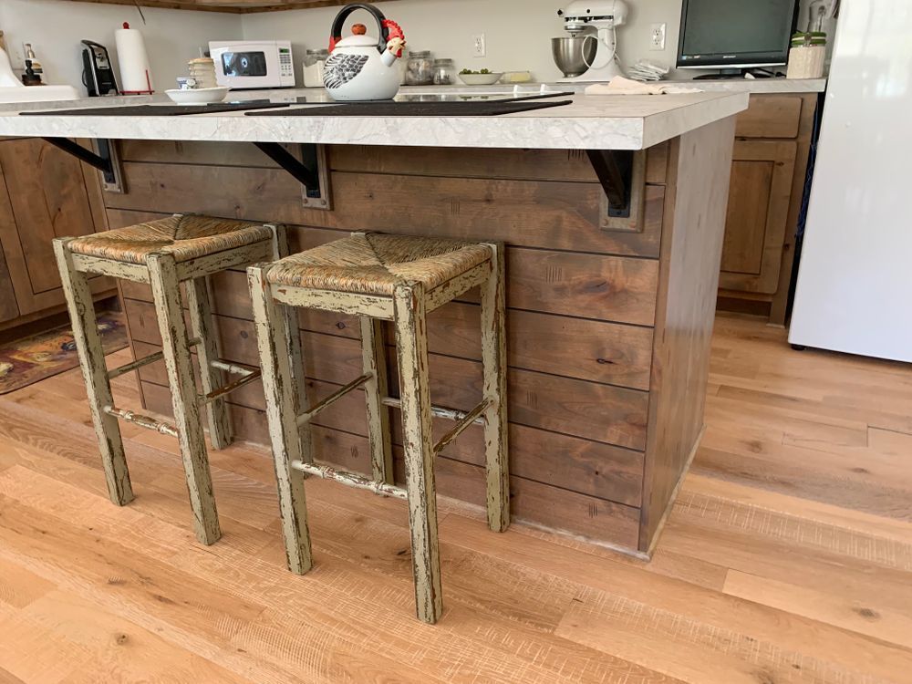 Kitchen island with distressed wood paneling and two bar stools, wooden floor.