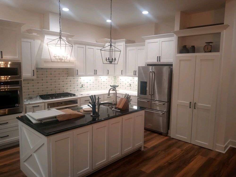 White kitchen with black countertops, stainless steel appliances, and dark wood floors.