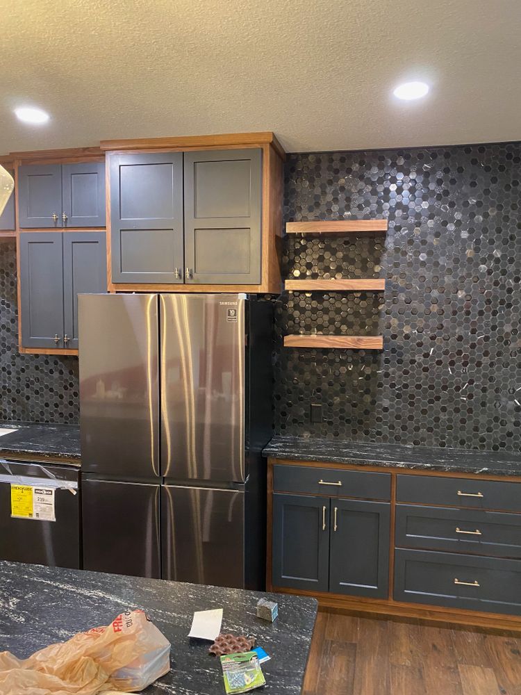 Kitchen with gray cabinets, stainless steel refrigerator, dark tiled backsplash, and wooden shelves.