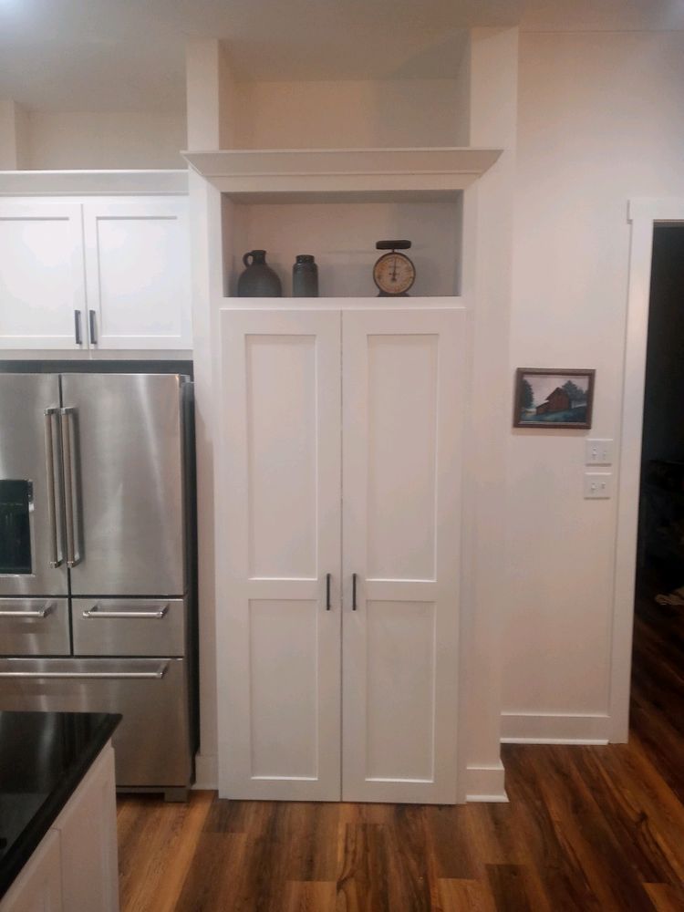 White pantry with open shelf holding decor, next to a stainless steel refrigerator in a kitchen.