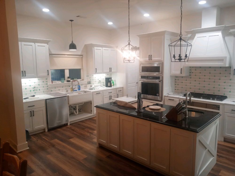White kitchen with island, cabinets, appliances, and dark countertops. Wooden floors and pendant lights.