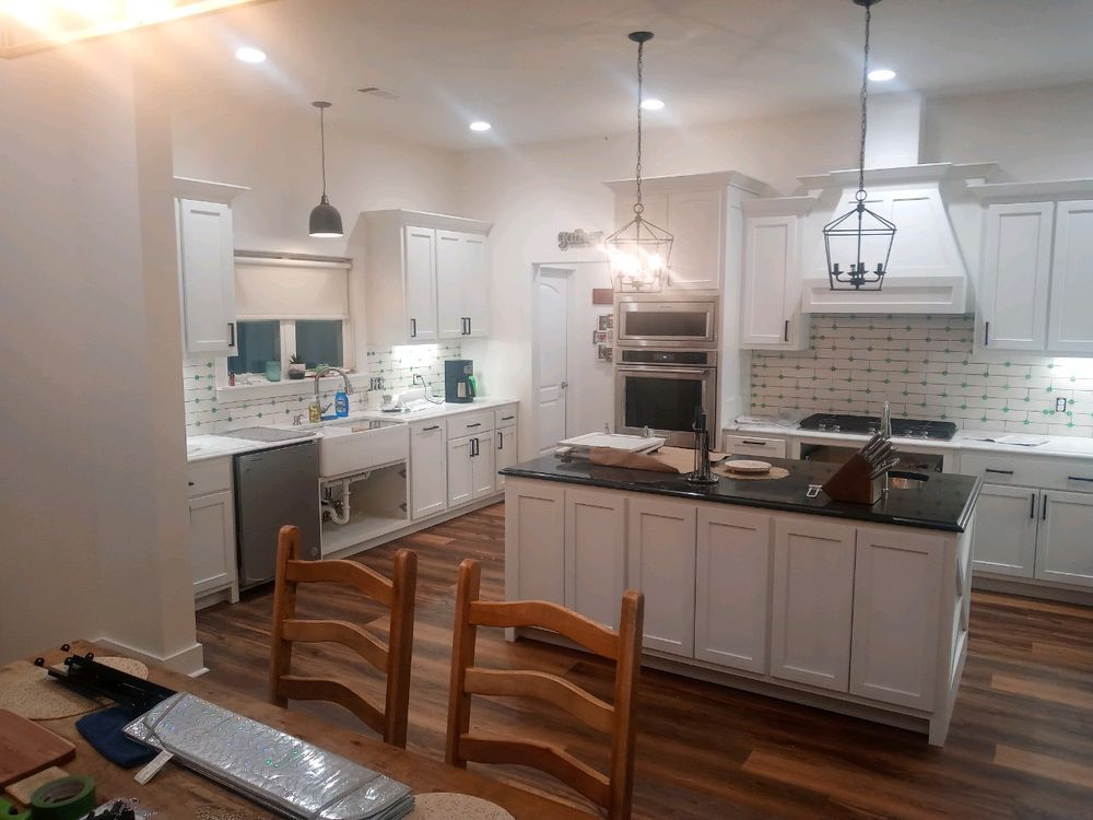 White kitchen with island, cabinets, appliances, and hardwood floors. Pendant lights hang above.