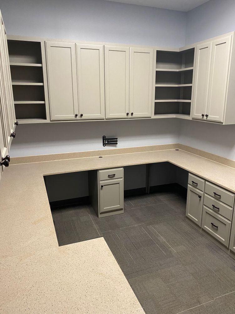 L-shaped office workspace with light cabinets and countertop, gray drawers, open shelving, and dark flooring.