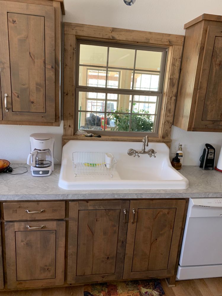 Kitchen with rustic wooden cabinets, a white sink under a window, and a white dishwasher.