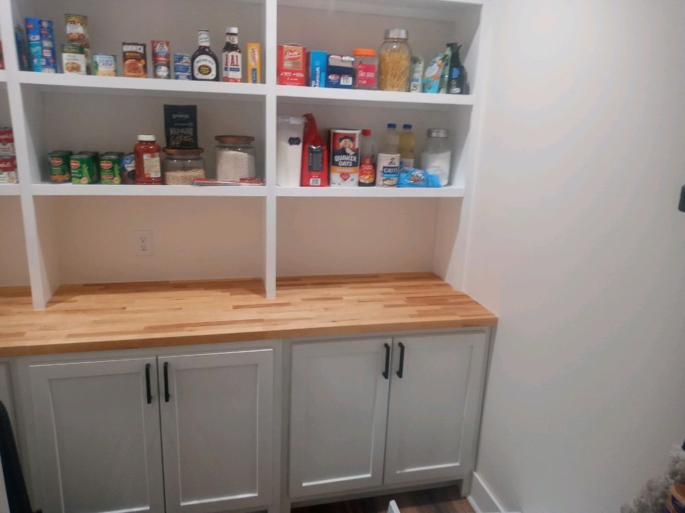 Pantry with white shelves, light wood countertop, and gray cabinets holding various food items.