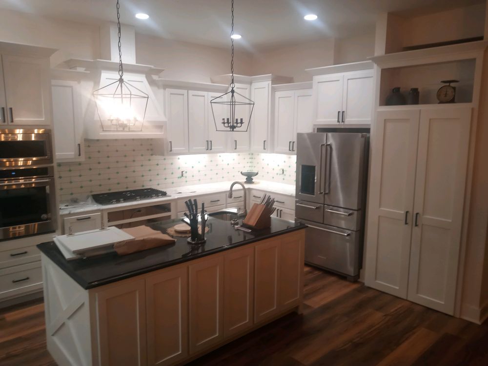 White kitchen with island and stainless steel appliances, dark countertops, and wood flooring.