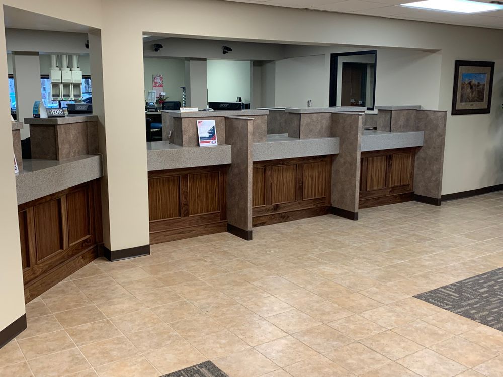 Bank teller counter with wood paneling, tan stone tops, and neutral tile flooring.