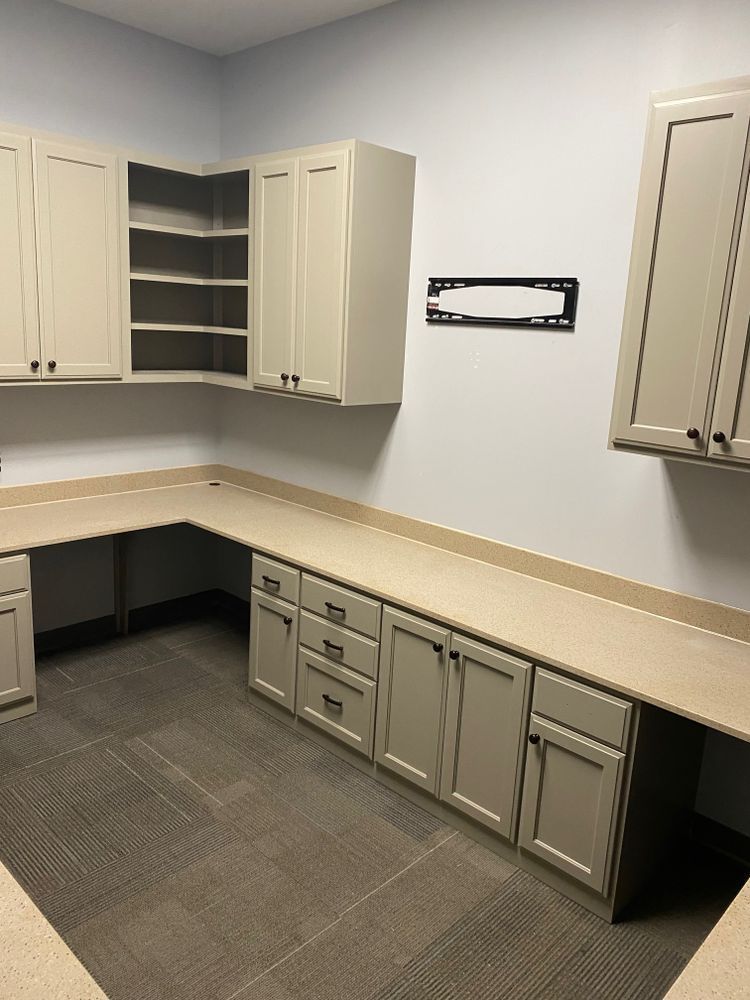 L-shaped built-in cabinets with a neutral countertop and light gray cabinets against a pale blue wall and gray carpet.