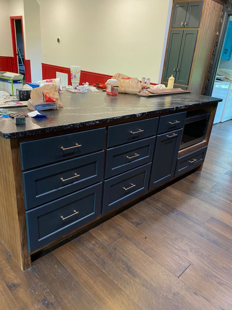 Kitchen island with dark blue cabinets, black countertop, microwave, and wood flooring.