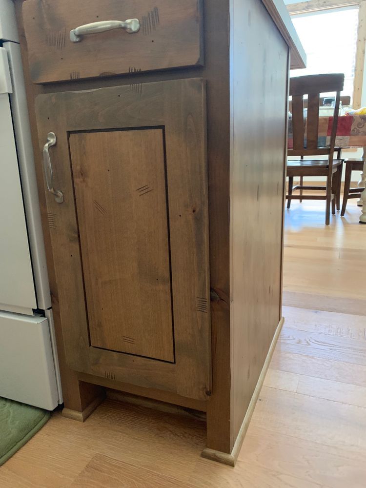 Wooden kitchen cabinet, two-tone stained, with drawer and door, on wood floor.