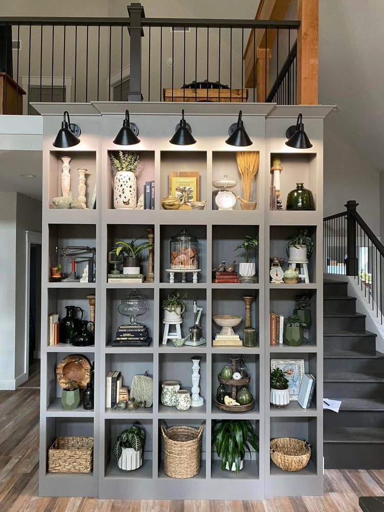 Gray built-in shelving unit with various decor, including plants and pottery. Black lights illuminate each shelf.
