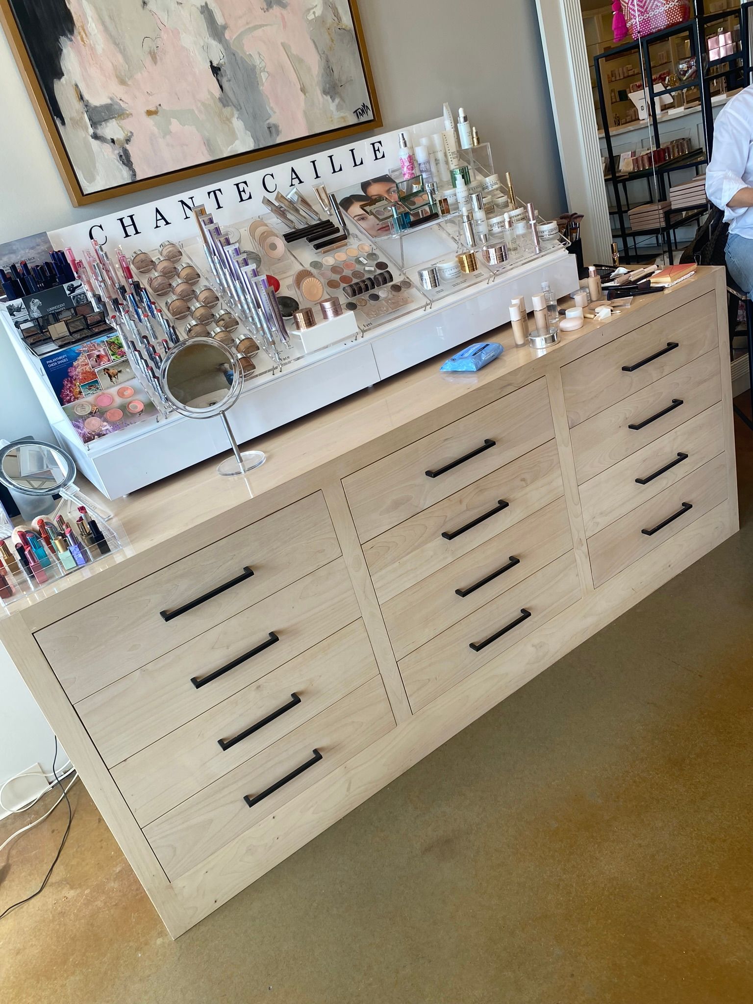 Wooden dresser with black handles, displaying jewelry and makeup products.