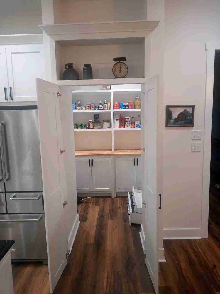 Open pantry with white doors and wooden floors, a stainless steel refrigerator, and built-in shelves.