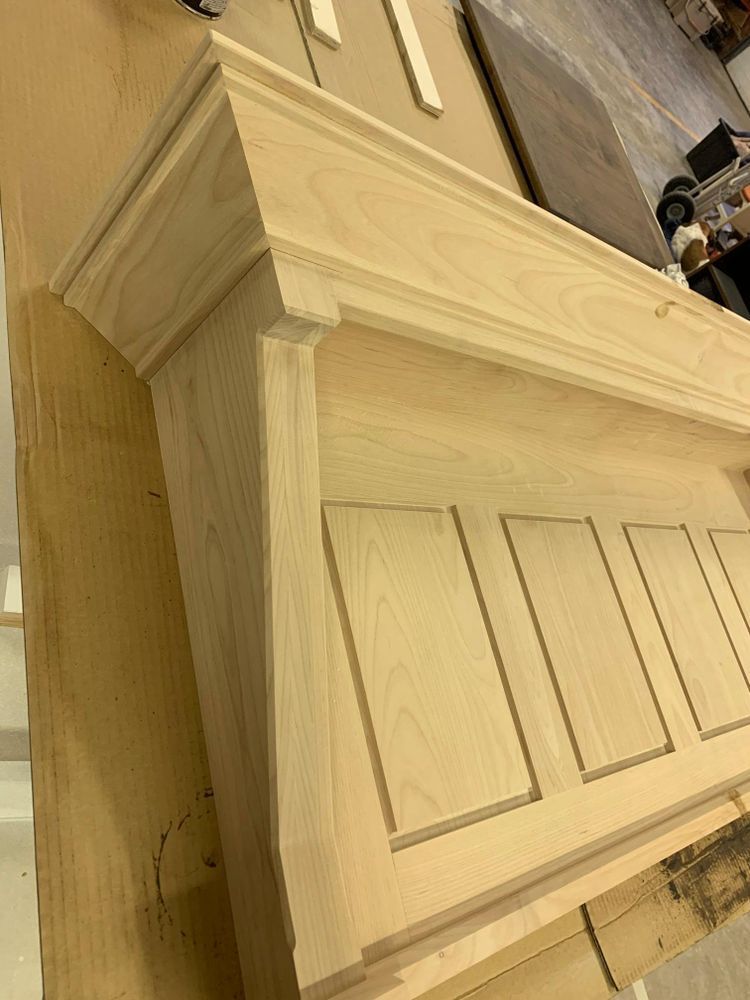 A wooden fireplace mantel under construction, with decorative panels and crown molding.