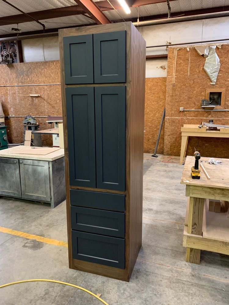 Tall wooden cabinet with dark blue doors and drawers in a workshop.
