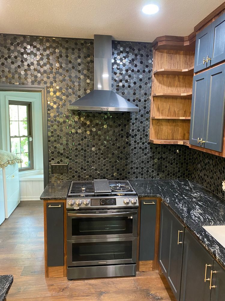 Kitchen with dark blue cabinets, stainless steel oven, hexagon tile backsplash, and wooden shelves.