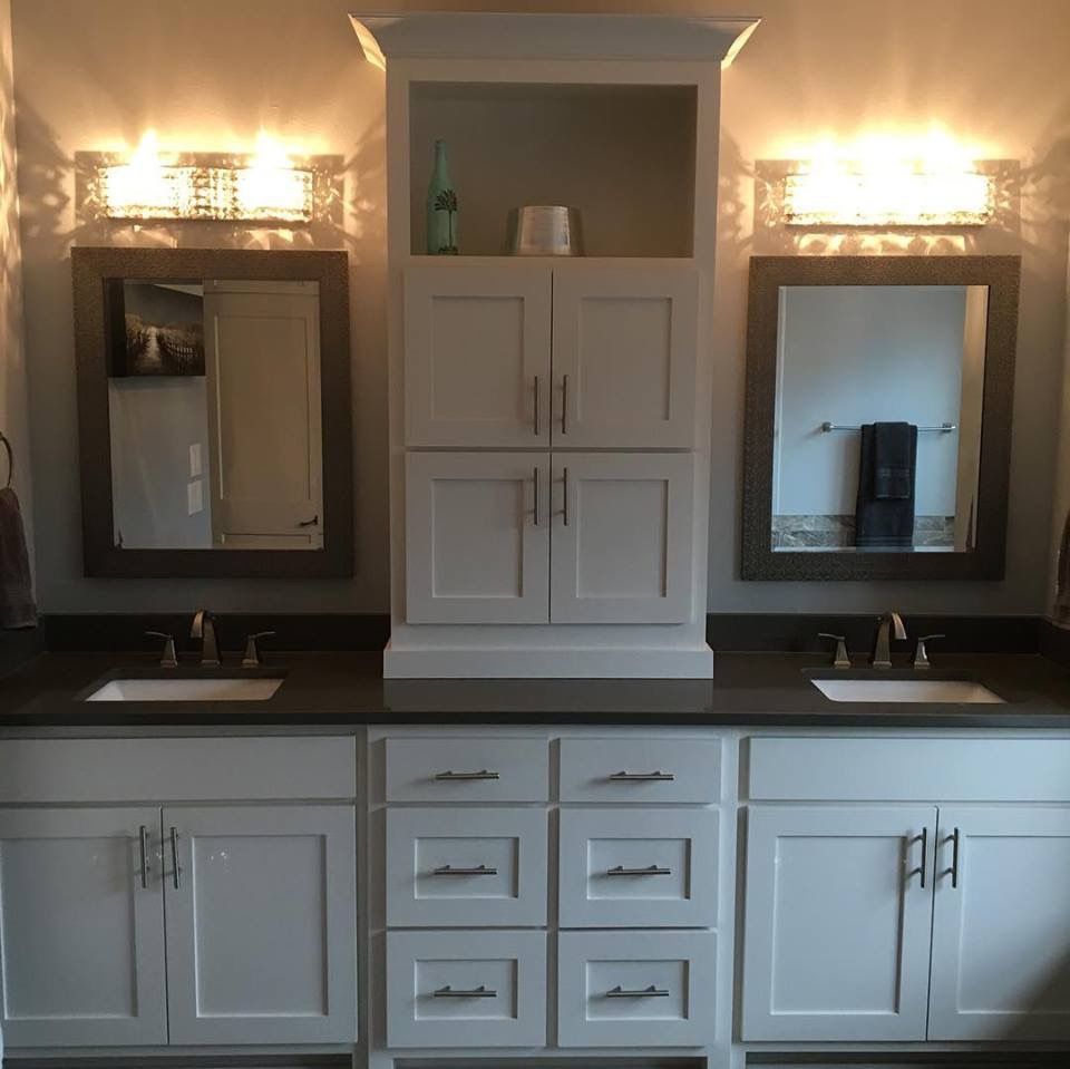 Bathroom with white cabinets, dark countertops, mirrors, and bright vanity lights.