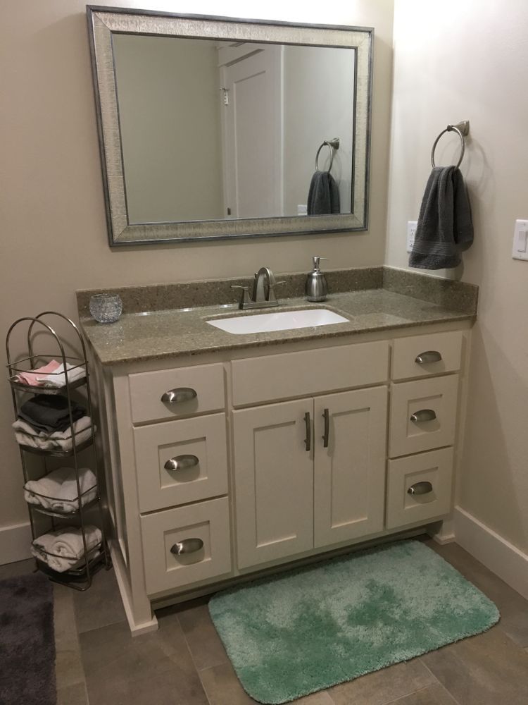 Bathroom vanity with white cabinet, granite countertop, mirror, and green bath mat.