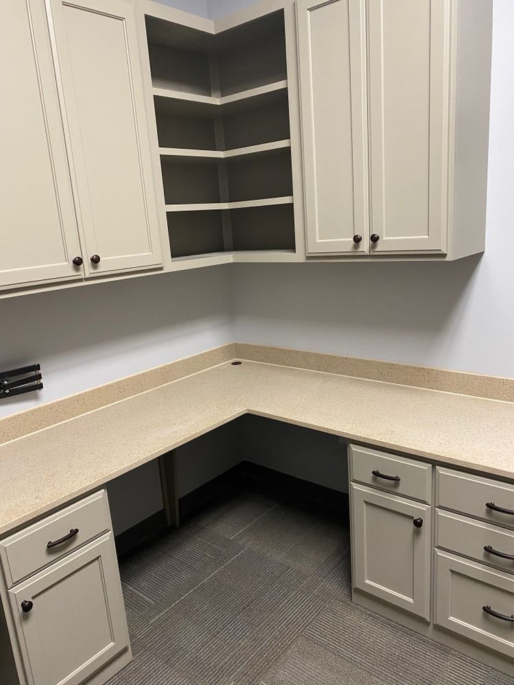 Built-in office desk with cabinets and open shelving; light tan surfaces and off-white cabinets.