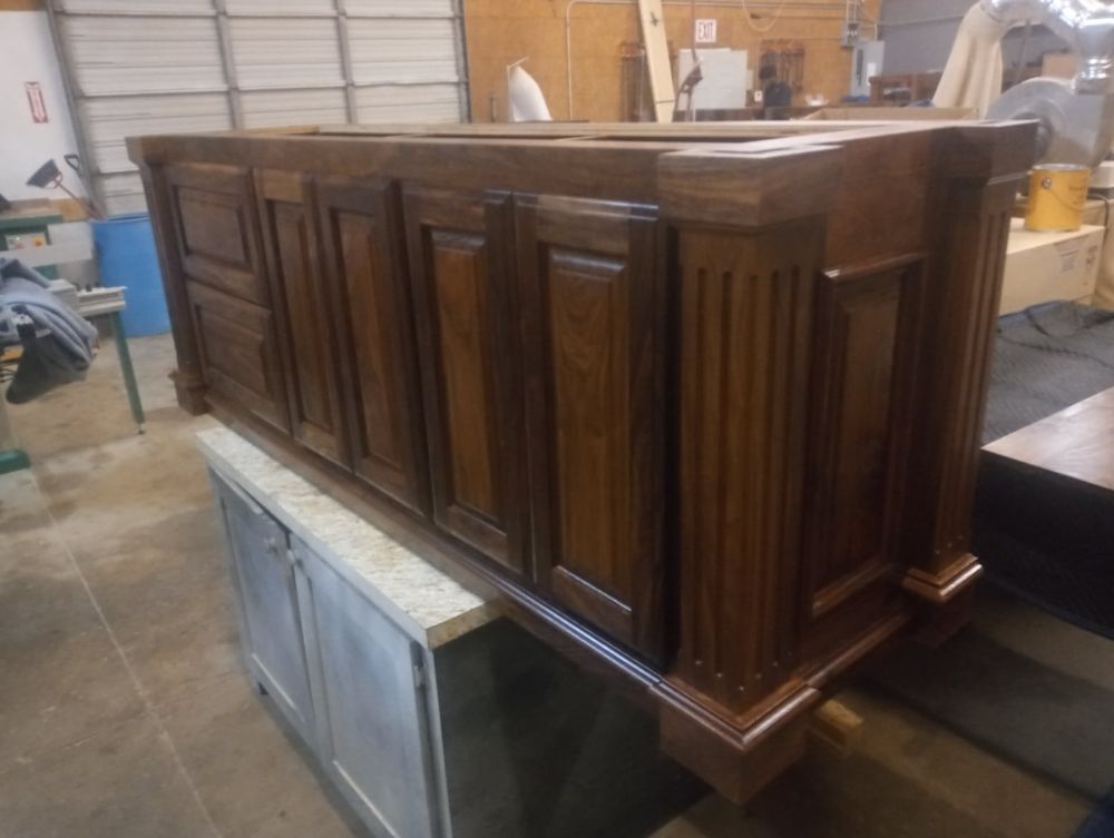 Wooden cabinet with columns and panel doors, finished in dark brown, sitting on a work surface.
