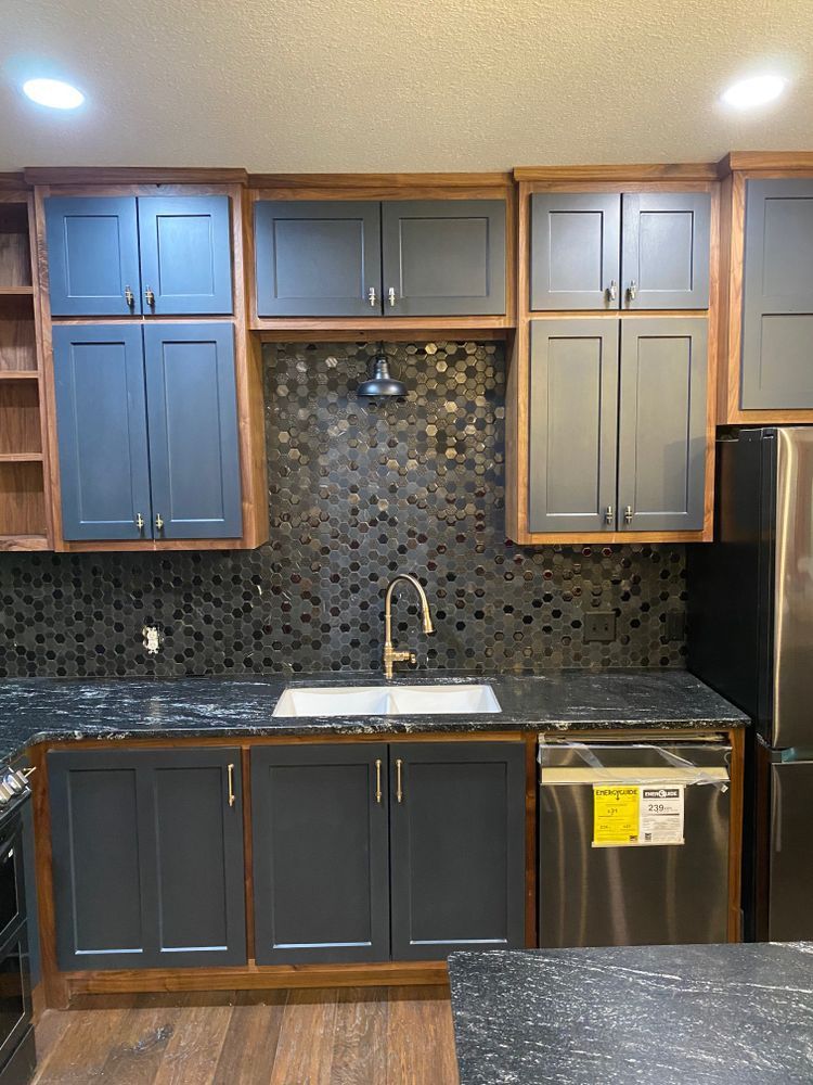 Kitchen with dark gray cabinets, wood trim, black backsplash, stainless steel appliances, and black countertop.