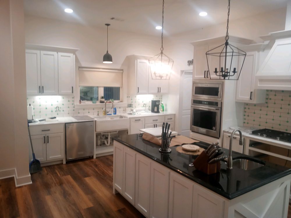 Modern white kitchen with island, black countertops, and pendant lights. Wood floor.