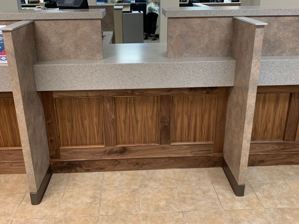 Customer service counter with light beige stone top and wooden front panels. Beige tile floor.