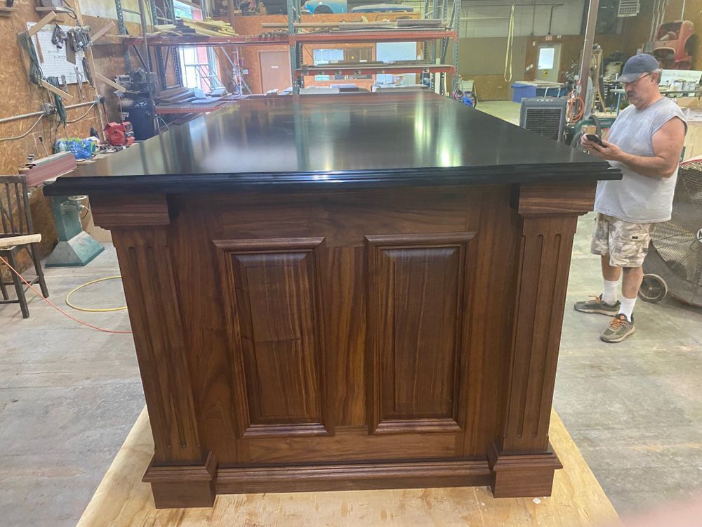Wooden bar with a dark countertop; a person is standing next to it.