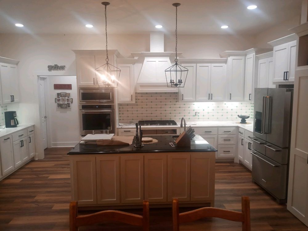 White kitchen with island and stainless steel appliances, dark countertop, and wood floors.