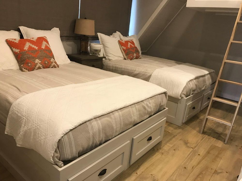 Two twin beds with white quilts and orange pillows in a room with a ladder to a top bunk.