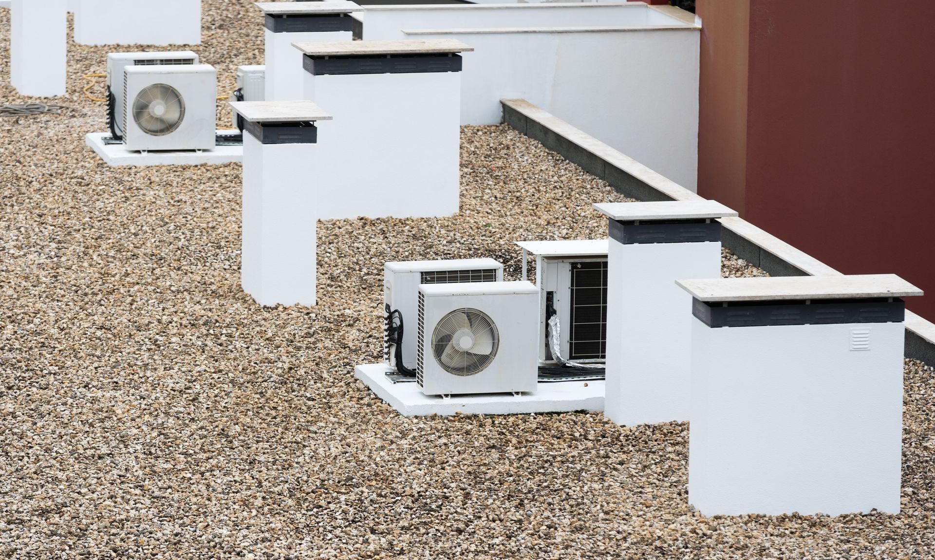 Outdoor row of white air conditioning units on a gravel rooftop.