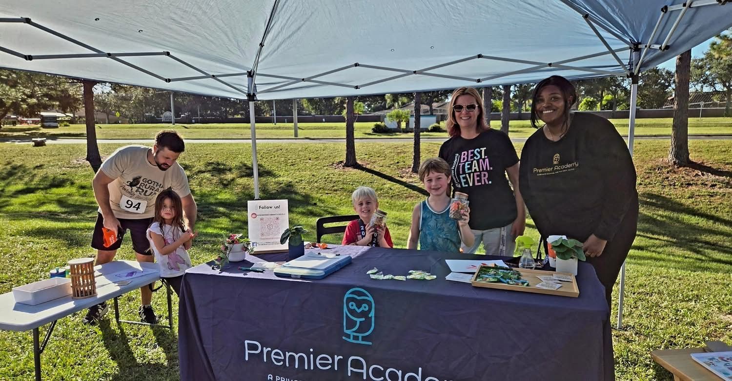 A group of people, including children and adults, are smiling under a blue canopy at an outdoor event.