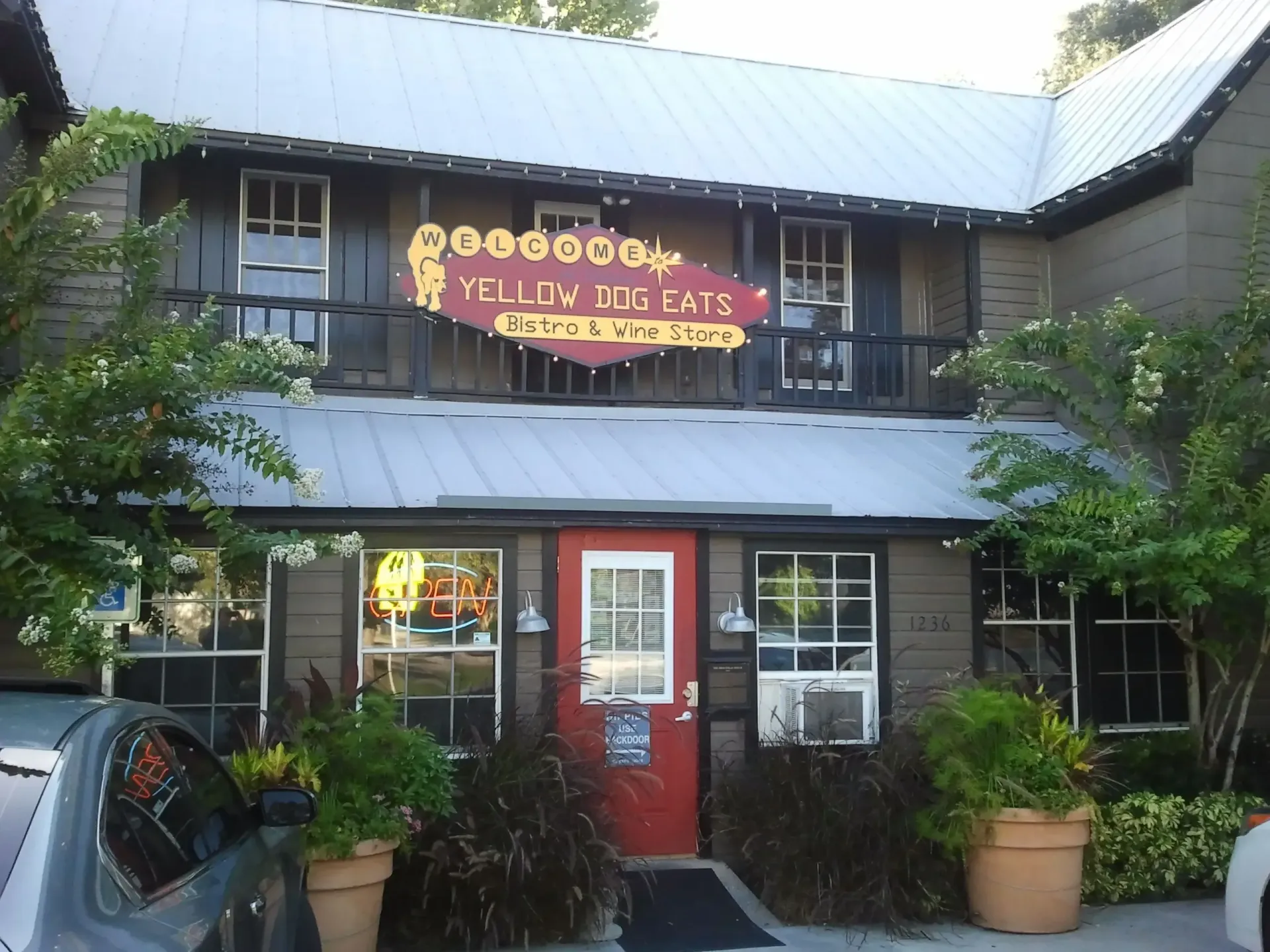 Yellow Dog Eats restaurant with red door, yellow sign, and plants.