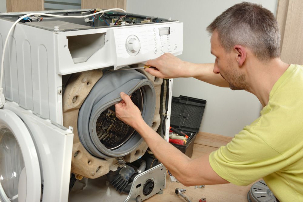 A Man is Fixing a Washing Machine in a Room —​ Centre Evap & Home Maintenance Services in Ciccone, NT