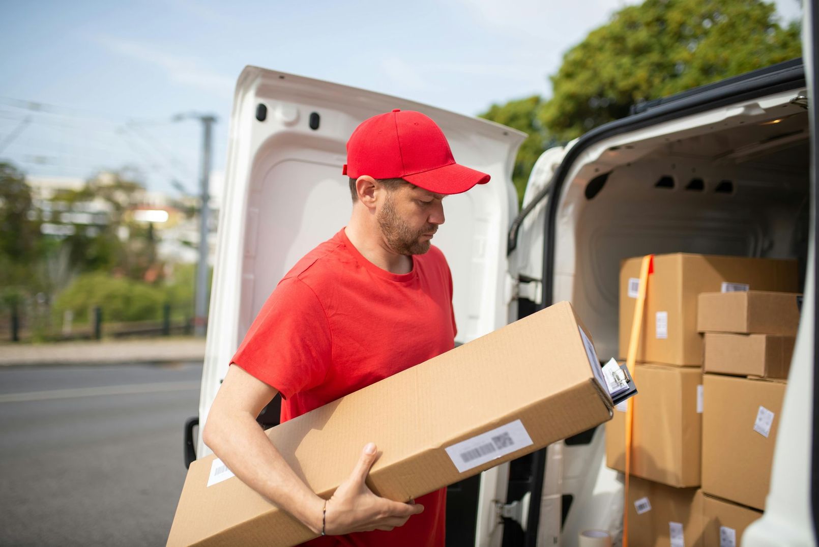 Repartidor con uniforme rojo cargando cajas de cartón en una furgoneta.